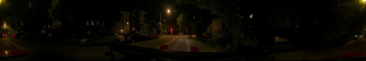 Glowing street lamps and a red traffic signal mark a tree-lined residential road in Washington, United States, during a clear spring night, seen from a car.