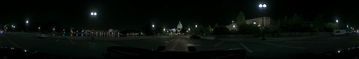 From a moving car, the illuminated United States Capitol appears at the end of a tree-lined road in Washington, United States, on a clear spring night.