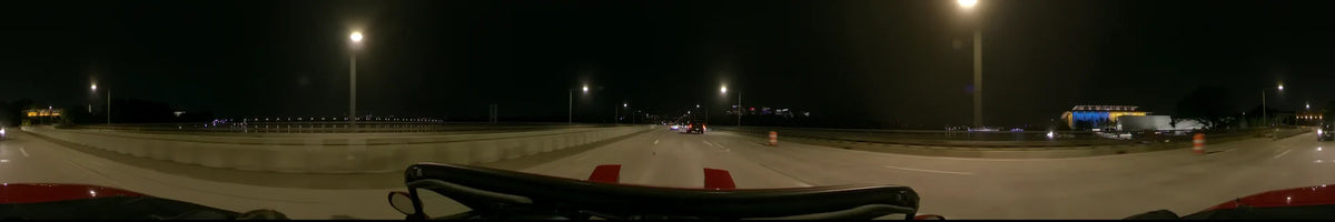 A car navigates a highway in Washington, United States, on a clear spring night, flanked by streetlamps, concrete barriers, and distant illuminated buildings.