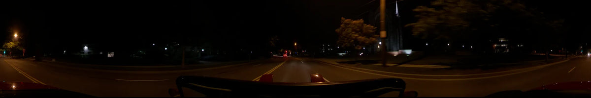 A red car drives through Washington, United States, on a clear spring night, moving along a dark road illuminated by distant street lamps.