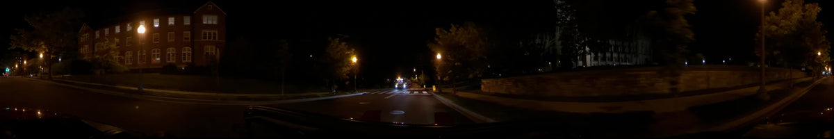 Flashing lights from a fire truck illuminate a crosswalk in Washington, United States, as a car drives by on a clear spring night under streetlamps.