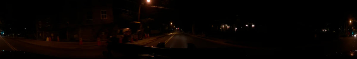 Orange traffic cones line the roadside during a clear spring night in Washington, United States, as a car follows another vehicle's red taillights.