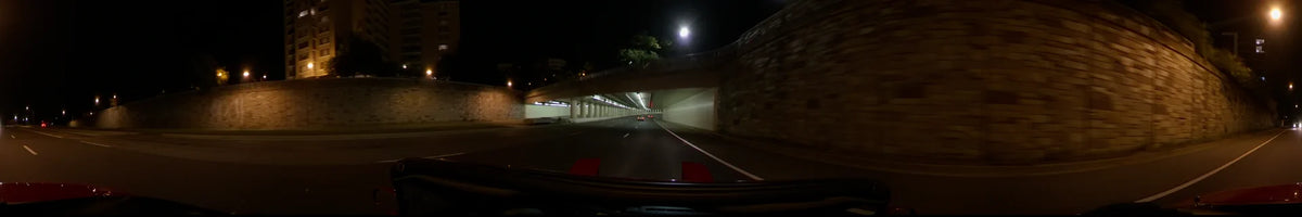 On a clear spring night in Washington, United States, a car passes beneath a concrete overpass, following red taillights through the lit underpass.