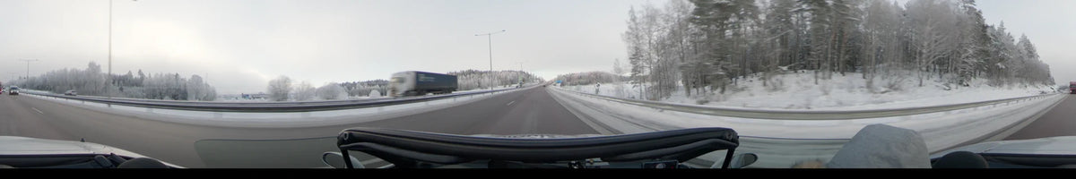 A car driving on a highway in Uppsala, Sweden, during an overcast winter day. The scene features snow-covered landscapes, street lights, and a passing truck.