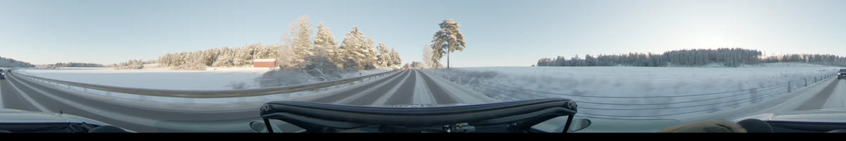 Frost-covered trees border a snowy road in Uppsala, Sweden, as a car drives through the landscape during a clear winter day.