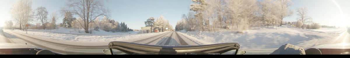 This daytime car view from Uppsala, Sweden, captures a snowy road and frost-covered trees under a clear winter sky, passing a small red building.
