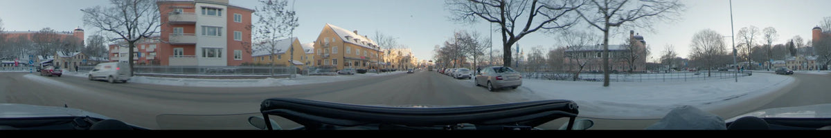 Yellow residential buildings and bare trees line a snowy city street in Uppsala, Sweden, as a car drives forward under a clear winter sky during the day.