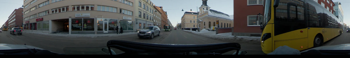 A silver car and a green bus appear on a snow-lined city street in Uppsala, Sweden, while a car drives by on a clear winter day.