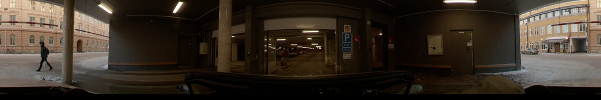 Entering a parking garage in Uppsala, Sweden, a car moves past concrete pillars and signage under fluorescent lights on a clear winter day.
